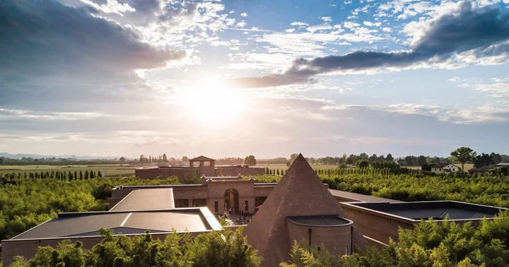 A brick pyramid and low buildings surrounded by a green bamboo maze under a wide, sunlit sky